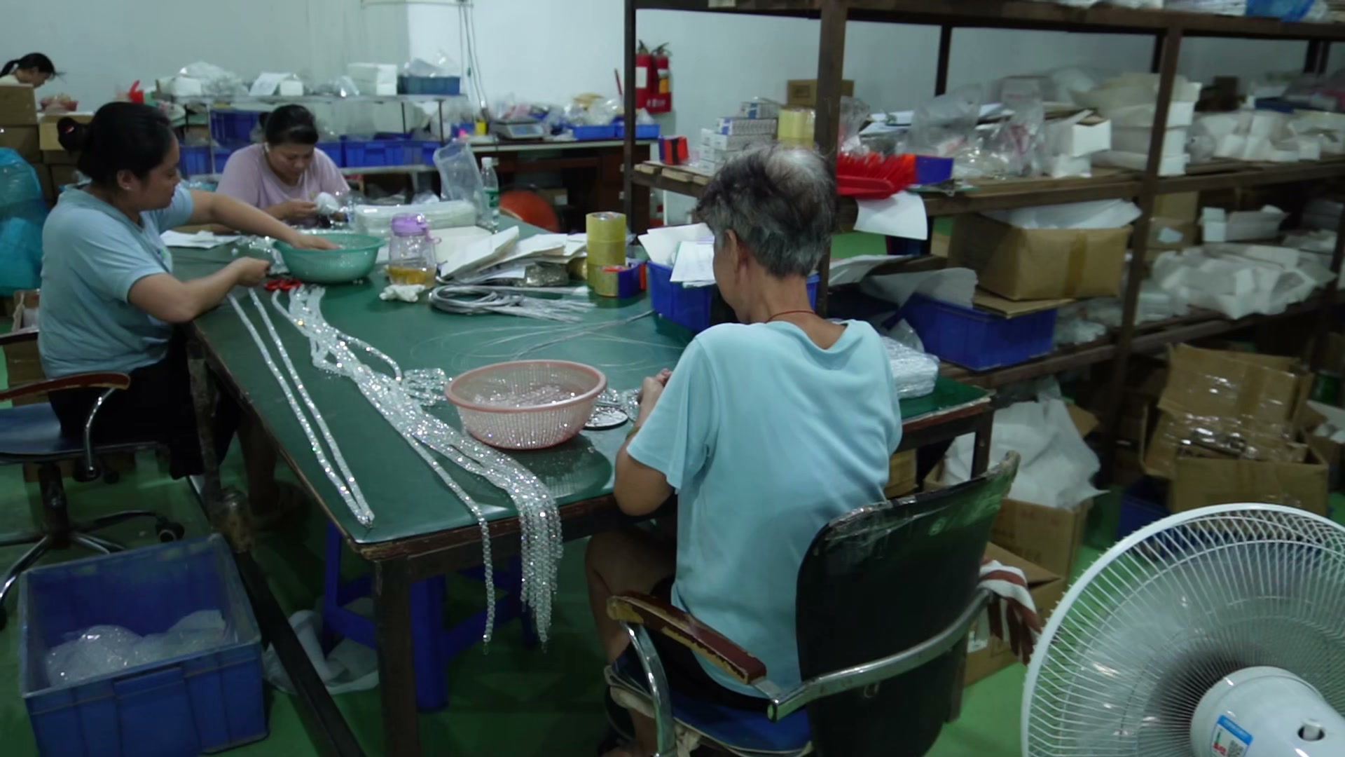 Hands arranging decorative strands at a workshop assembly table