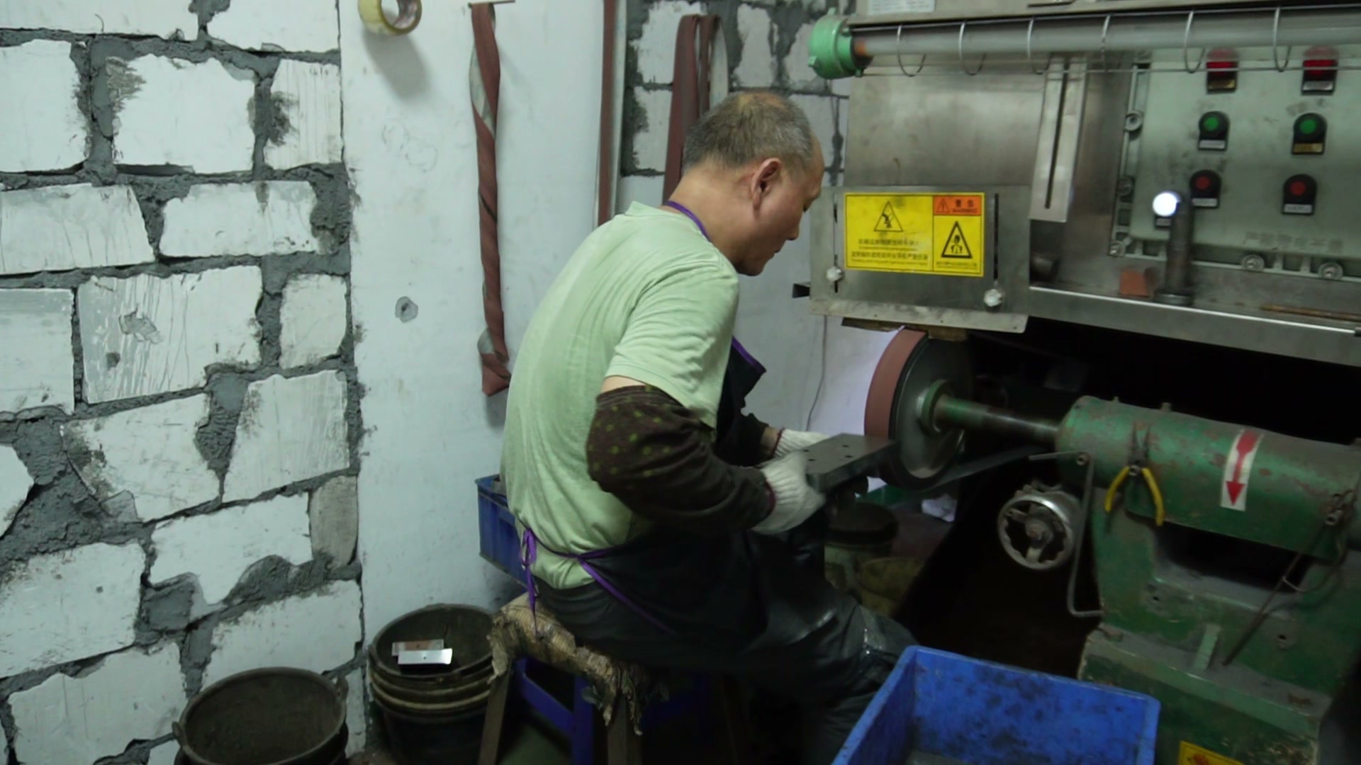 Worker holding a metal part against a polishing wheel